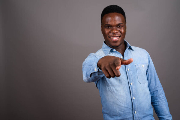 Studio shot of young African man wearing denim shirt against gray background
