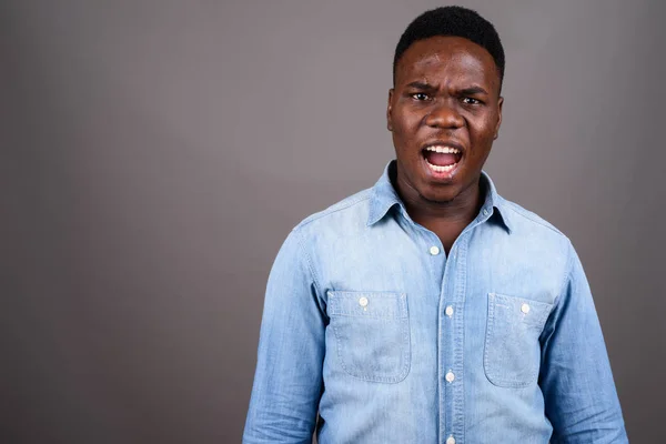 Young African man wearing denim shirt against gray background — Stock Photo, Image