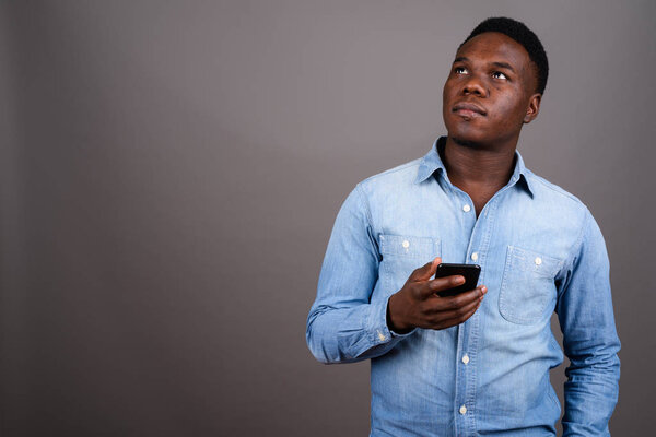 Studio shot of young African man using mobile phone against gray background