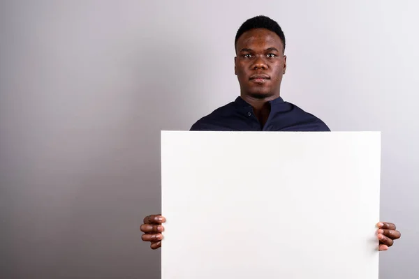 Jovem empresário africano segurando placa branca contra costas brancas — Fotografia de Stock
