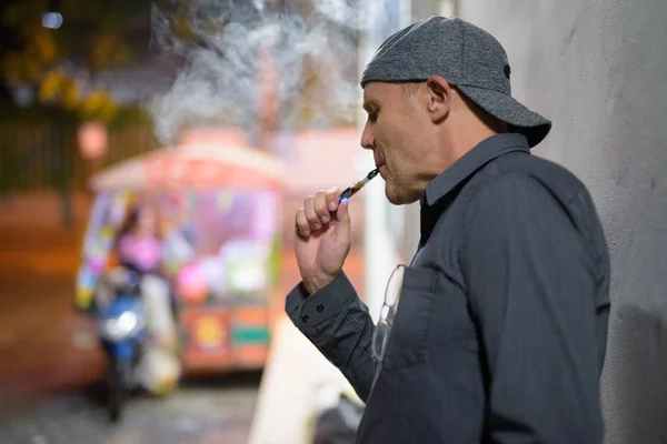 Зрелый мужчина, курящий электронные сигареты на улицах ночью — стоковое фото