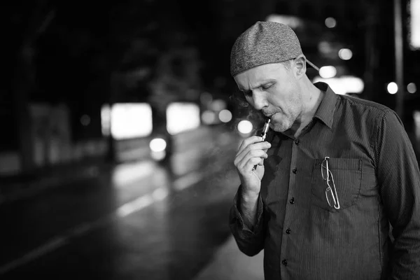 Gammal man röker elektronisk cigarett på gatorna på natten — Stockfoto