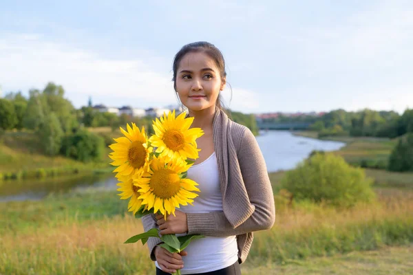 Doordachte jonge mooie Aziatische vrouw bedrijf boeket van zonnebloemen tegen ontspannen uitzicht op natuur — Stockfoto