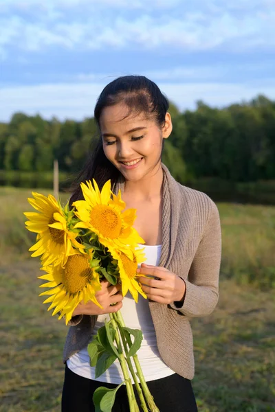 Joven mujer asiática feliz sosteniendo ramo de girasoles contra relajante vista de la naturaleza —  Fotos de Stock