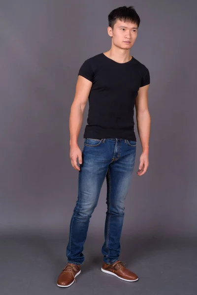 Studio shot of young Chinese man against gray background — Stock Photo, Image