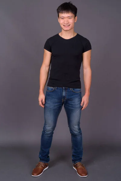 Studio shot of young Chinese man against gray background — Stock Photo, Image