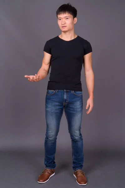 Studio shot of young Chinese man against gray background — Stock Photo, Image