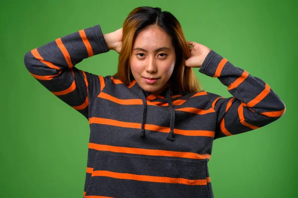 Portret van jonge Aziatische vrouw tegen groene achtergrond — Stockfoto