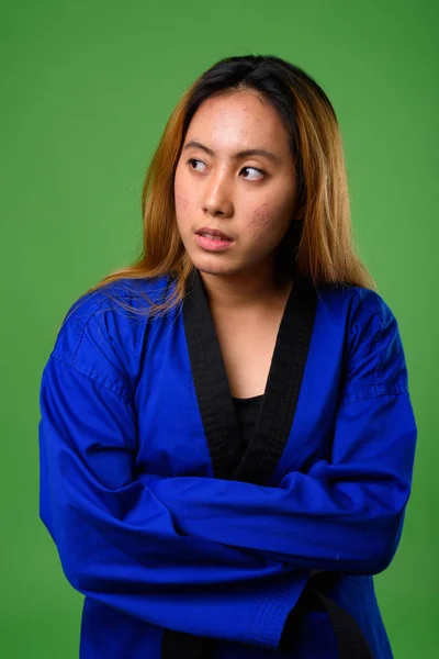 Joven mujer asiática vistiendo karate azul Gi contra fondo verde —  Fotos de Stock