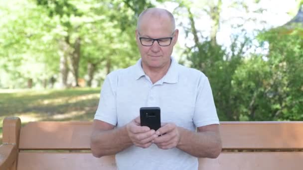 Buon uomo anziano pensando durante l'utilizzo del telefono al parco — Video Stock