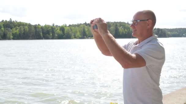 Heureux homme âgé enregistrement vidéo avec téléphone près du lac — Video