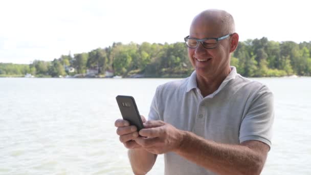 Feliz homem sênior usando telefone perto do lago — Vídeo de Stock