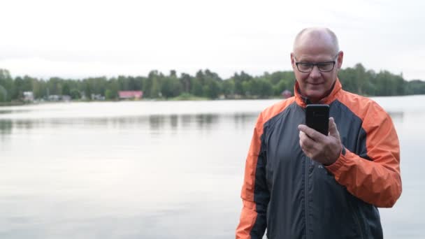 Pomocí telefonu šťastný starší muž a myšlení u jezera — Stock video