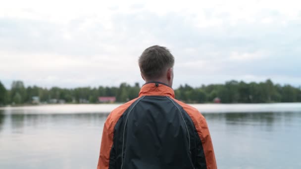 Задній вид молодий чоловік, насолоджуючись видом на озеро — стокове відео