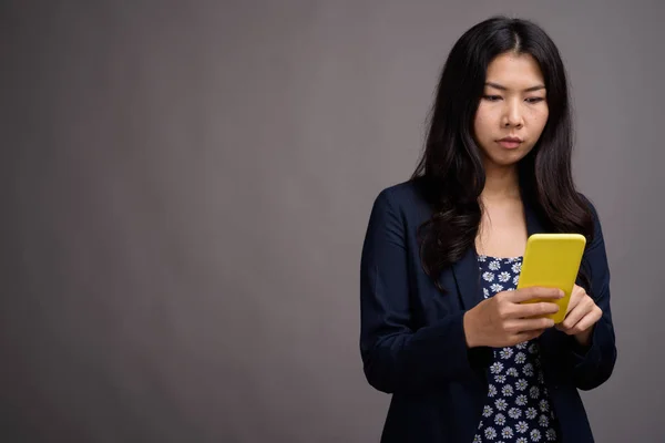 Asian woman using mobile phone against gray background — Stock Photo, Image