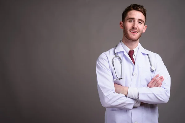Mladý pohledný muž lékař na šedém pozadí — Stock fotografie