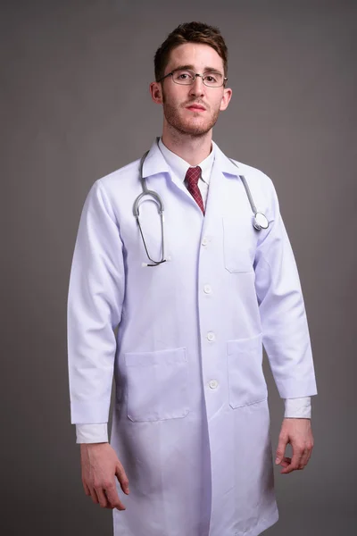 Jóképű fiatalember orvos visel szemüveget szürke háttérben ellen — Stock Fotó