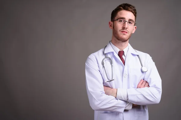 Jovem bonito homem médico vestindo óculos contra backgr cinza — Fotografia de Stock