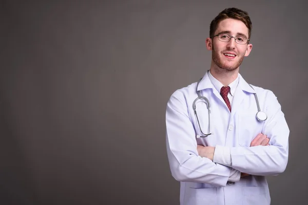Mladý pohledný muž lékař nosit brýle proti šedé pozadí — Stock fotografie