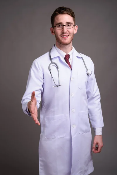 Jovem bonito homem médico vestindo óculos contra backgr cinza — Fotografia de Stock