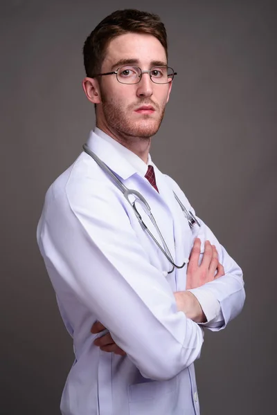 Junger schöner Mann Arzt trägt Brille gegen grauen Backgr — Stockfoto