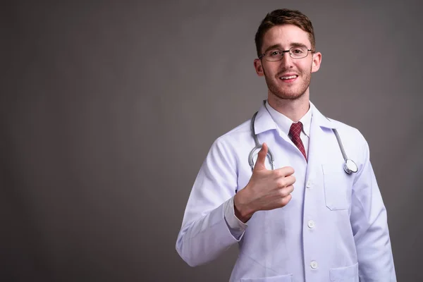 Jeune homme beau médecin portant des lunettes contre backgr gris — Photo