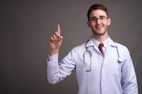 Mladý pohledný muž lékař nosit brýle proti šedé pozadí — Stock fotografie