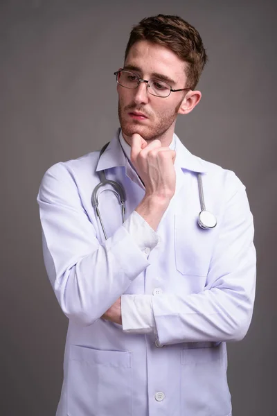 Jóképű fiatalember orvos visel szemüveget szürke háttérben ellen — Stock Fotó