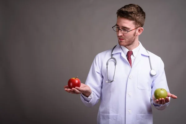 Giovane bell'uomo medico indossa occhiali contro sfondo grigio — Foto Stock