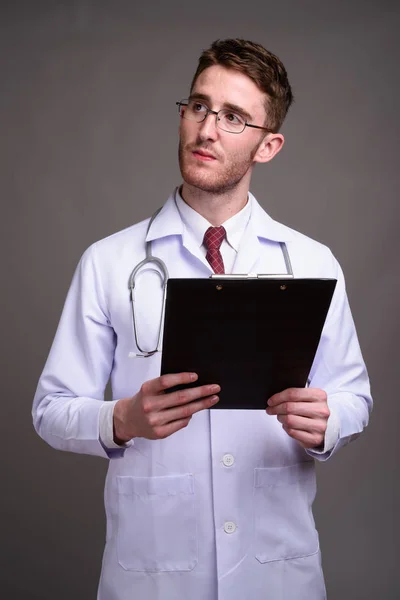 Giovane bell'uomo medico indossa occhiali contro sfondo grigio — Foto Stock