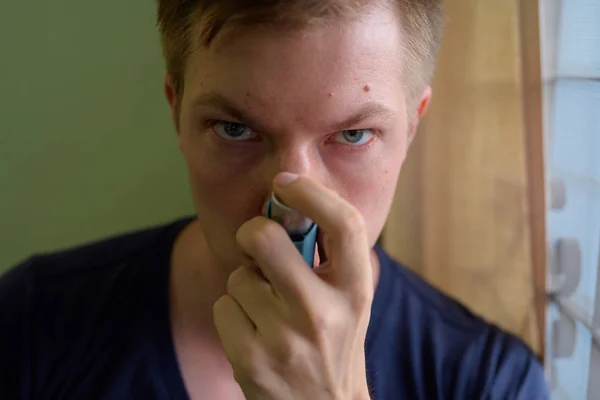 Νεαρός όμορφος άντρας που χρησιμοποιεί συσκευή εισπνοής άσθματος στο σπίτι — Φωτογραφία Αρχείου
