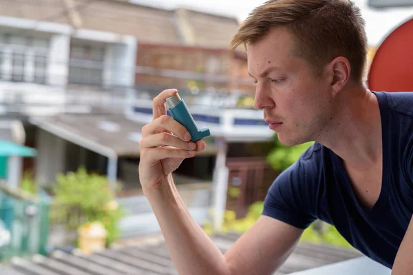 Young handsome man using asthma inhaler at home — Stock Photo, Image