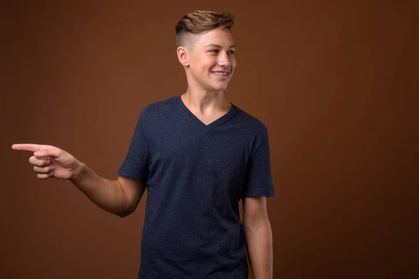 Studio shot of young handsome teenage boy against brown backgrou — Stock Photo, Image