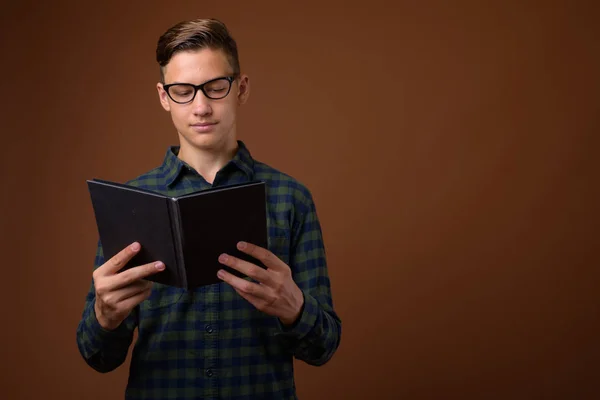 Studio shot of young handsome teenage boy against brown backgrou — Stock Photo, Image