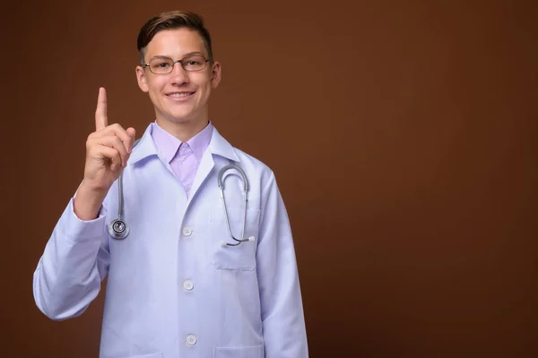 Studio colpo di giovane bel medico contro sfondo marrone — Foto Stock