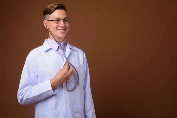 Studio záběr mladý pohledný doktor proti hnědým pozadím — Stock fotografie
