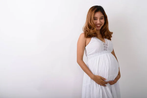 Studio shot of young happy Asian pregnant woman smiling while ho — Stock Photo, Image