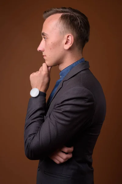 Studio shot of young handsome businessman against brown backgrou — Stock Photo, Image