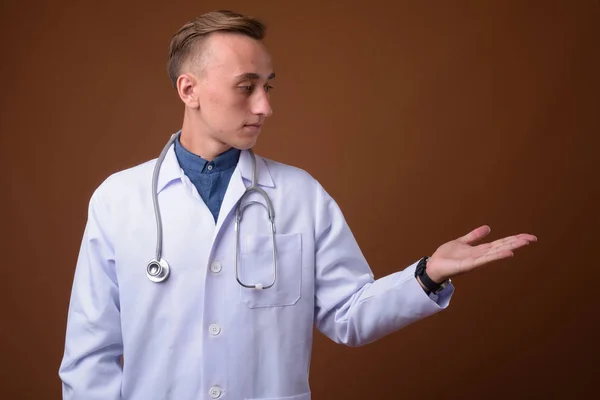 Junger schöner Mann Arzt vor braunem Hintergrund — Stockfoto