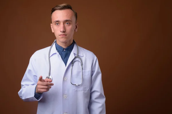 Joven hombre guapo médico contra fondo marrón —  Fotos de Stock