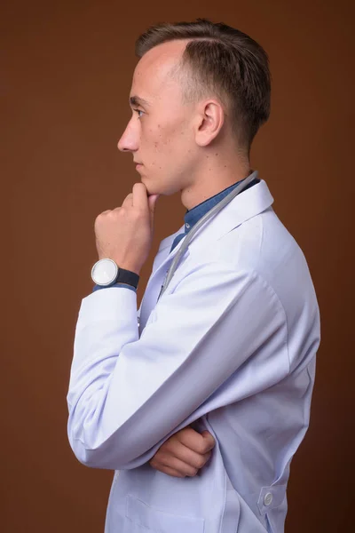 Joven hombre guapo médico contra fondo marrón —  Fotos de Stock