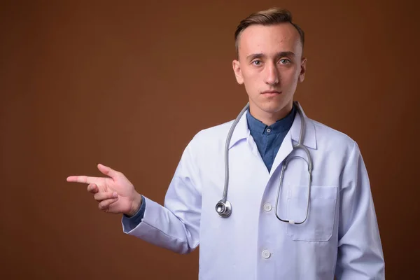 Junger schöner Mann Arzt vor braunem Hintergrund — Stockfoto