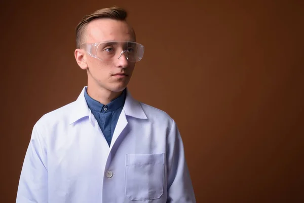 Jongeman wetenschapper arts tegen bruine achtergrond — Stockfoto