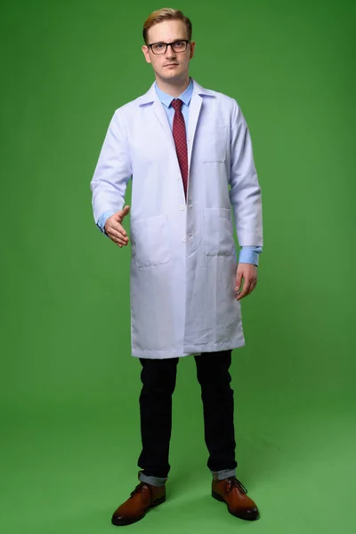 Junger schöner Mann Arzt mit blonden Haaren vor grünem Hintergrund — Stockfoto