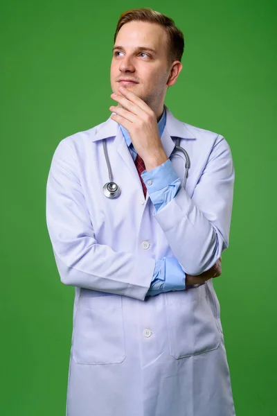 Junger schöner Mann Arzt mit blonden Haaren vor grünem Hintergrund — Stockfoto
