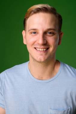 Sarı saçlı, yeşil arka planda genç yakışıklı bir adam.