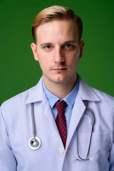 Young handsome man doctor with blond hair against green backgrou — Stock Photo, Image