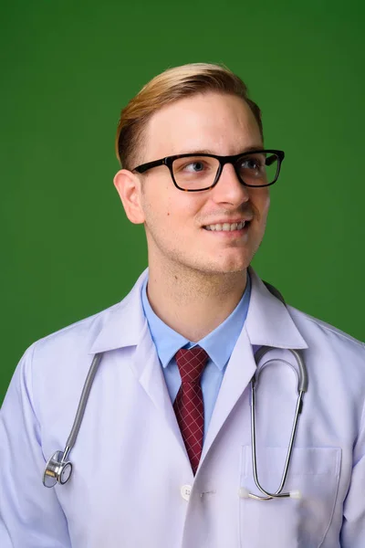 Jovem médico homem bonito com cabelo loiro contra backgrou verde — Fotografia de Stock