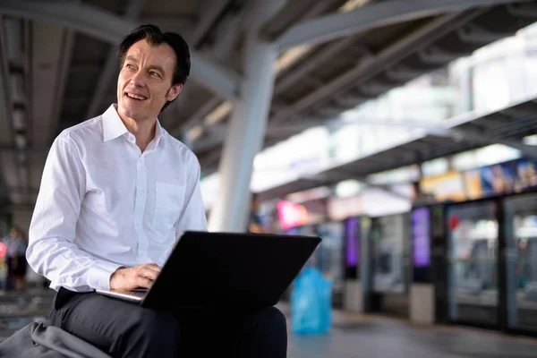 Зрелый красивый бизнесмен, использующий ноутбук на вокзале — стоковое фото