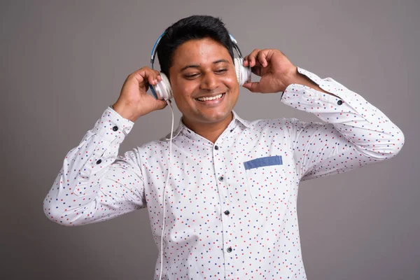 Young Indian businessman listening to music against gray backgro